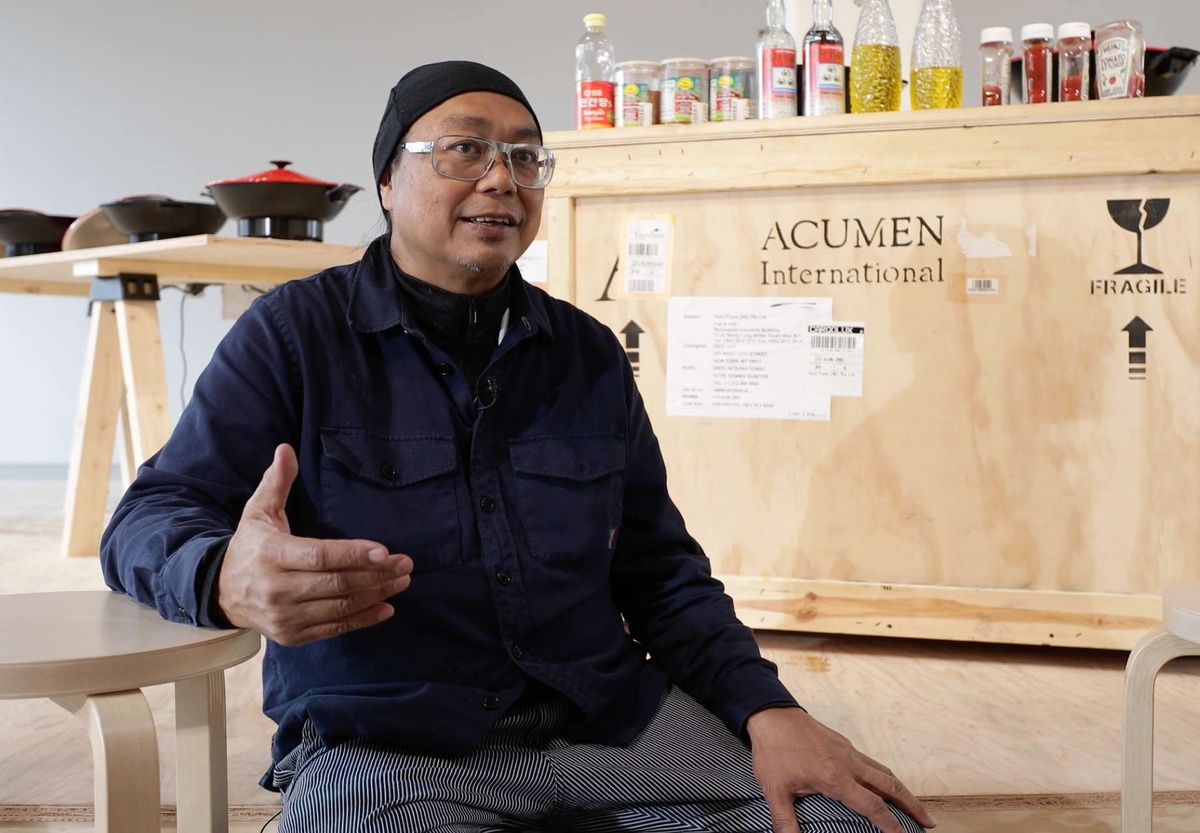 Rirkrit Tiravanija sits in front of his installation at MoMA PS1