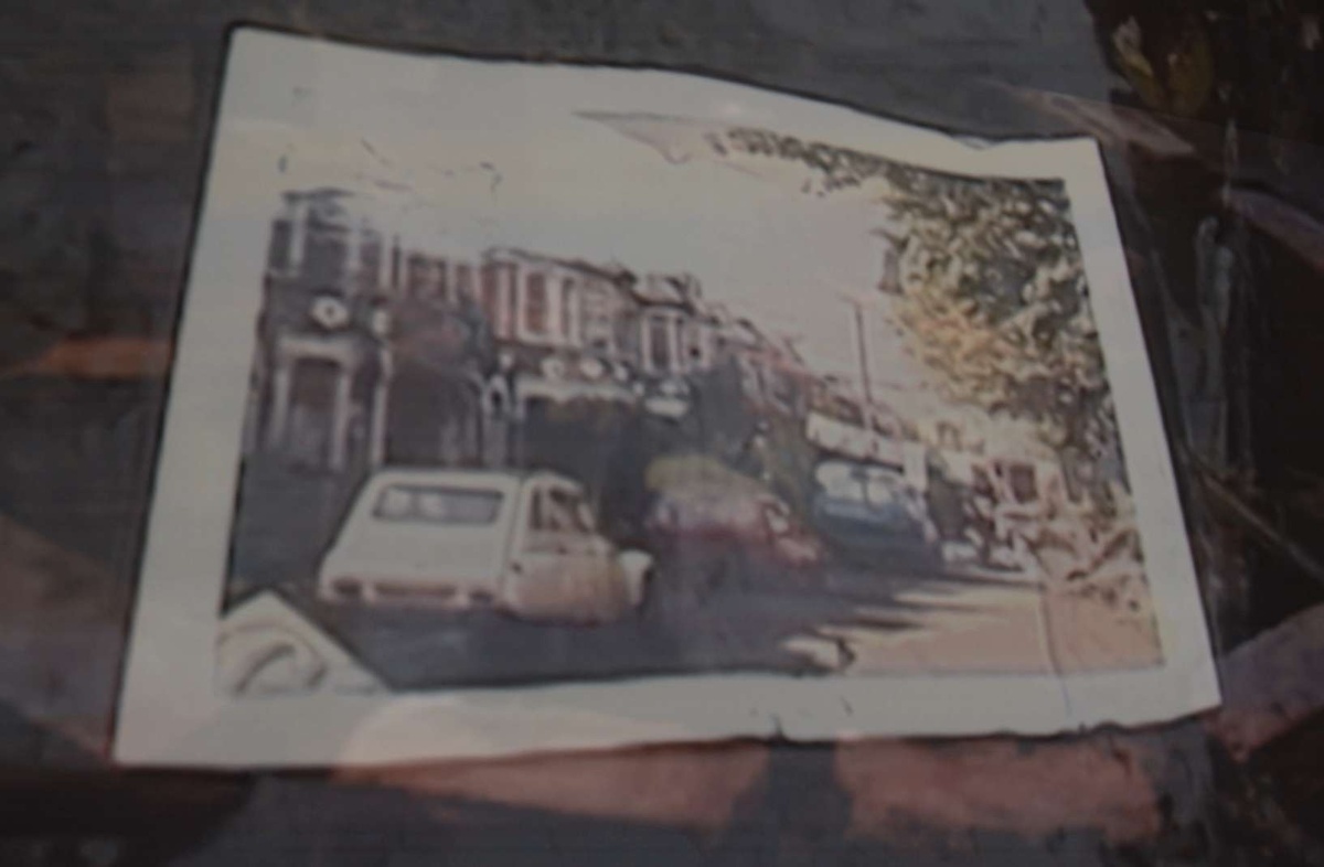 graint photograph of a newspaper spread on a desk. the paper has a full page image of a street with cars.