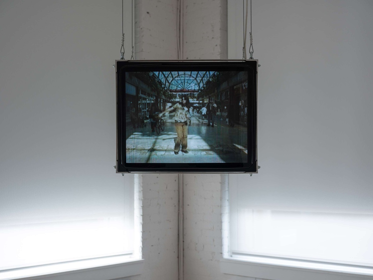 A television suspended television shows an image of a woman dancing in the middle of a shopping mall.