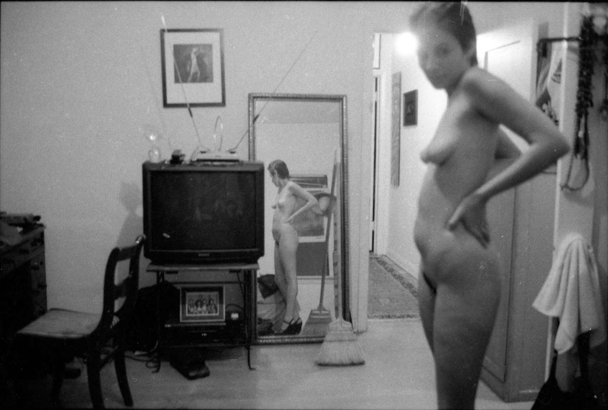 A black and white photograph taken by Reynaldo Rivera of a person standing naked in heels before a mirror.
