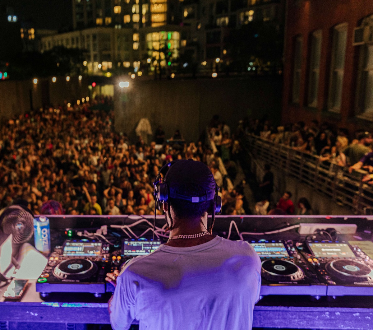A DJ stands before a crowded outdoor dance floor at MoMA PS1's Warm Up.