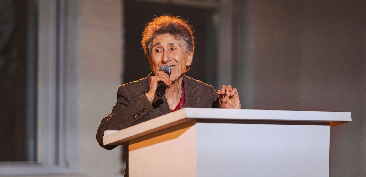 Silvia Federici smiles on stage as she holds a microphone. 