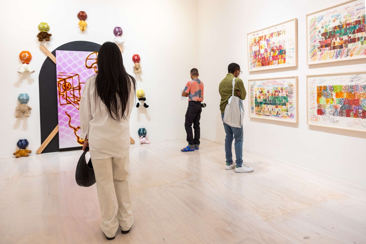 Three people stand throughout a white-walled gallery viewing artworks.