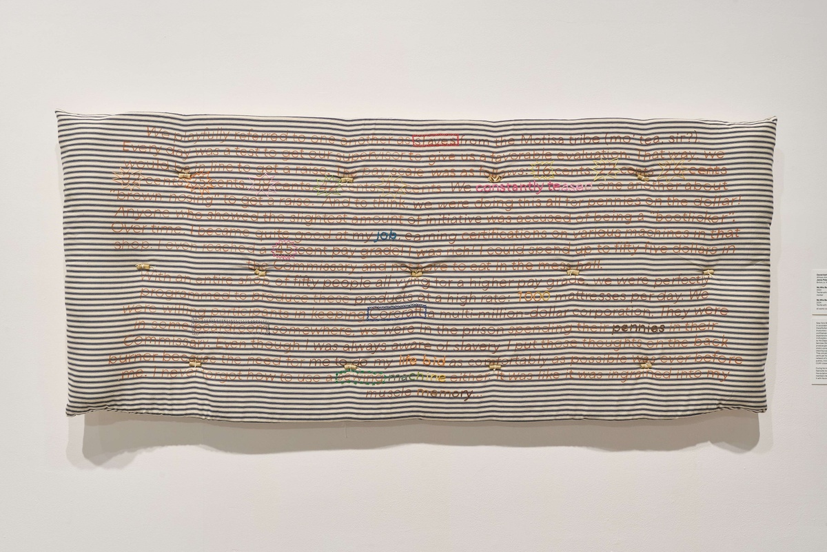 A prison mattress attached to a gallery wall, covered in writing.