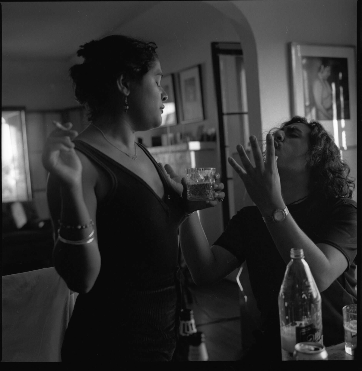 Two people face one another around a table in a black and white photo by Reynaldo Rivera. They may be fighting or singing—we can't tell—but their familiarity hangs in the air.