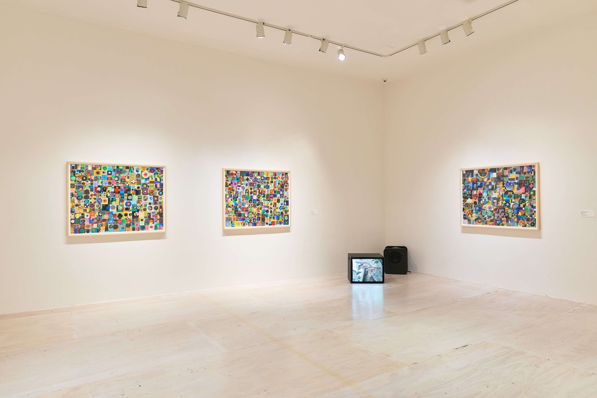 Three pieces of colorful artwork hang on the gallery walls, a CRT television set sits on the floor.