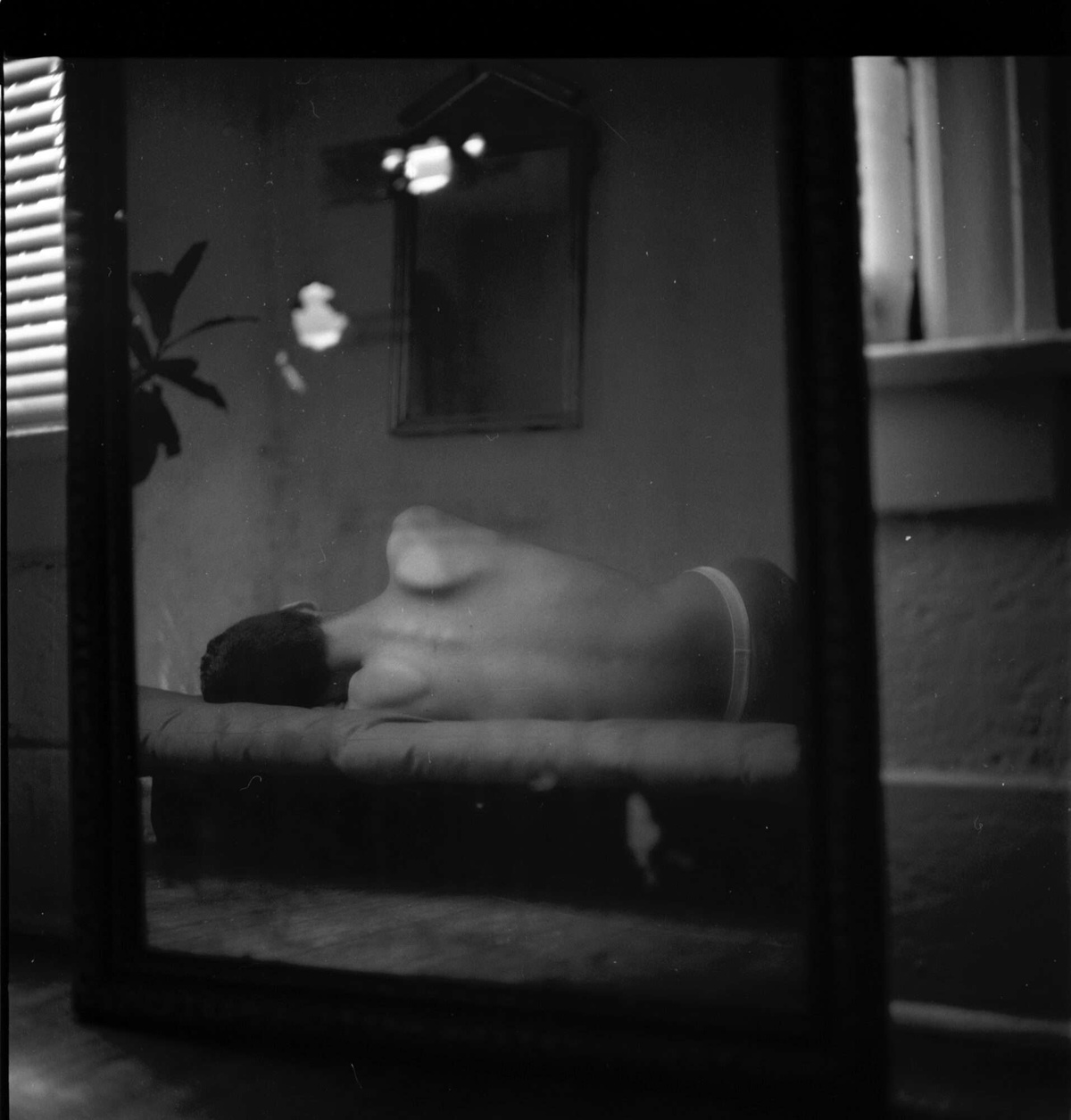 The arching scapula of a person laying on a bed is reflected in a mirror in a black and white photo by Reynaldo Rivera. 