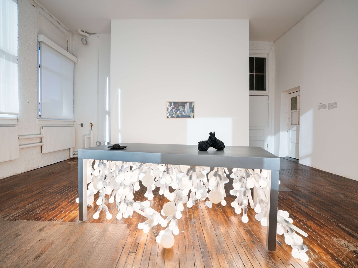 A metal table illuminated by dozens of lightbulbs underneath. Two small black sculptures sit on top of the table.