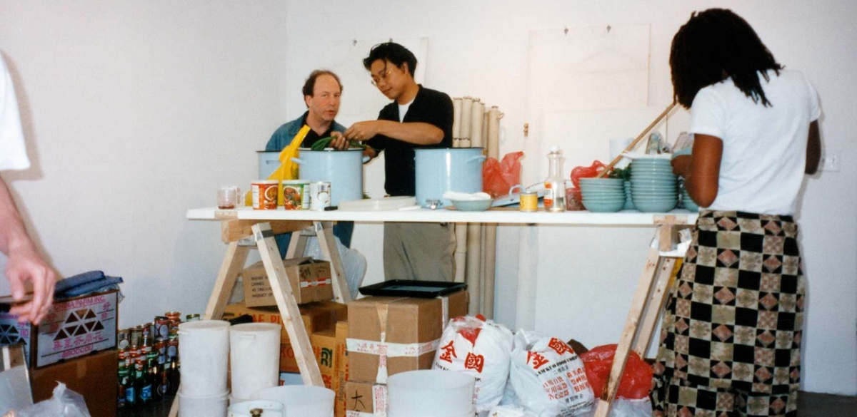 Rirkrit Tiravanija stands at a table cooking Thai curry