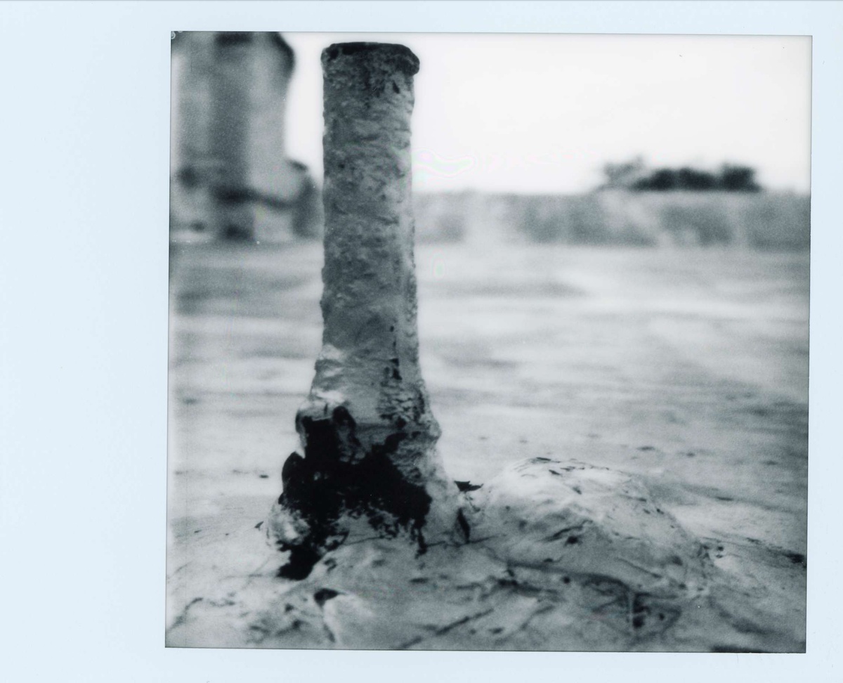 Black and white polaroid of a rooftop. A strange, chimney-like form emerges from the foreground.