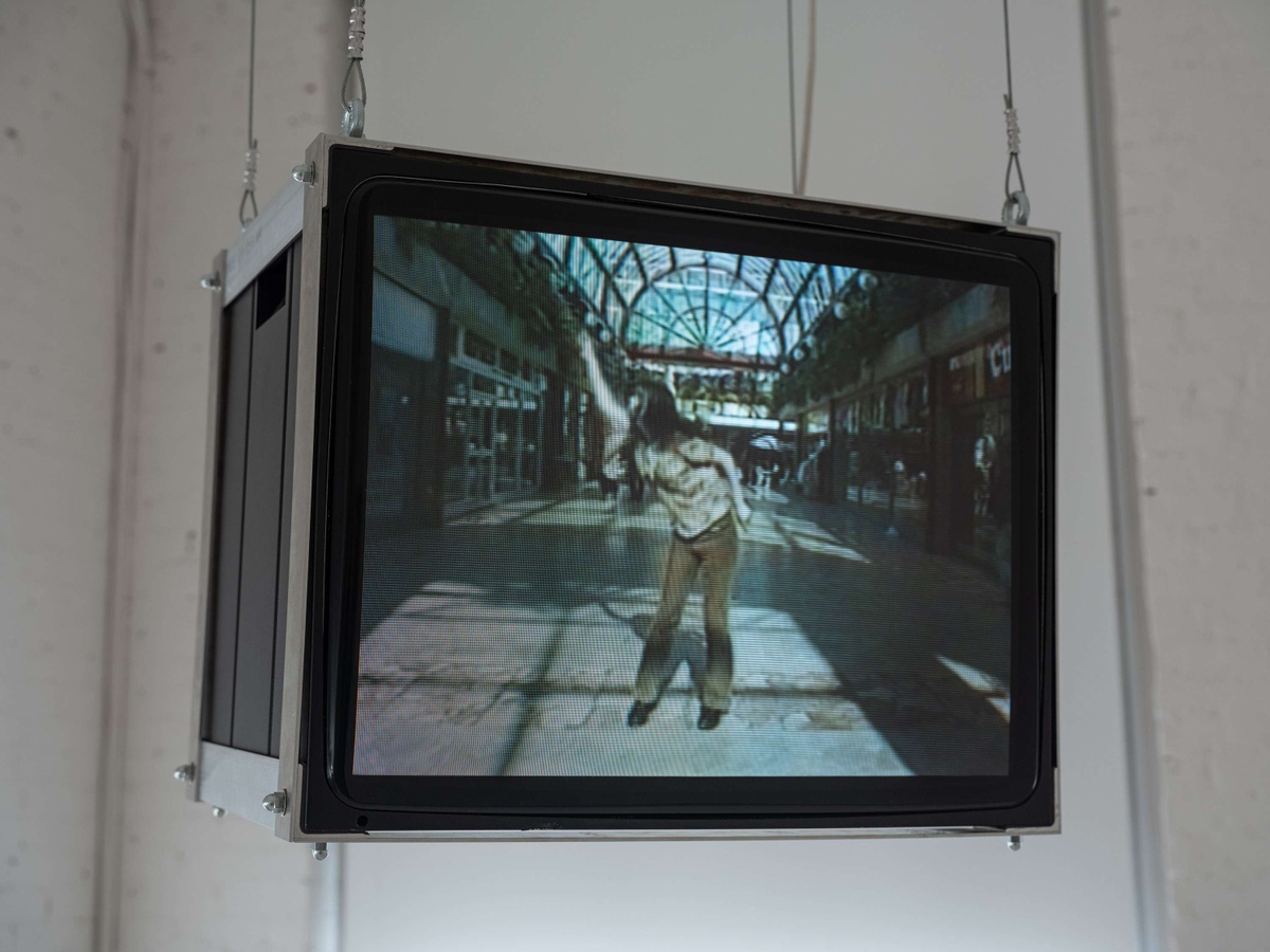 A television suspended television shows an image of a woman dancing in the middle of a shopping mall.