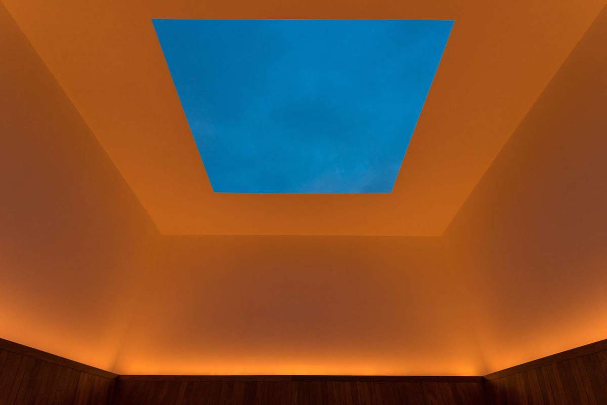 An installation by James Turrell is comprised of room lit in orange light with a massive square cut into the ceiling revealing a blue slice of sky.
