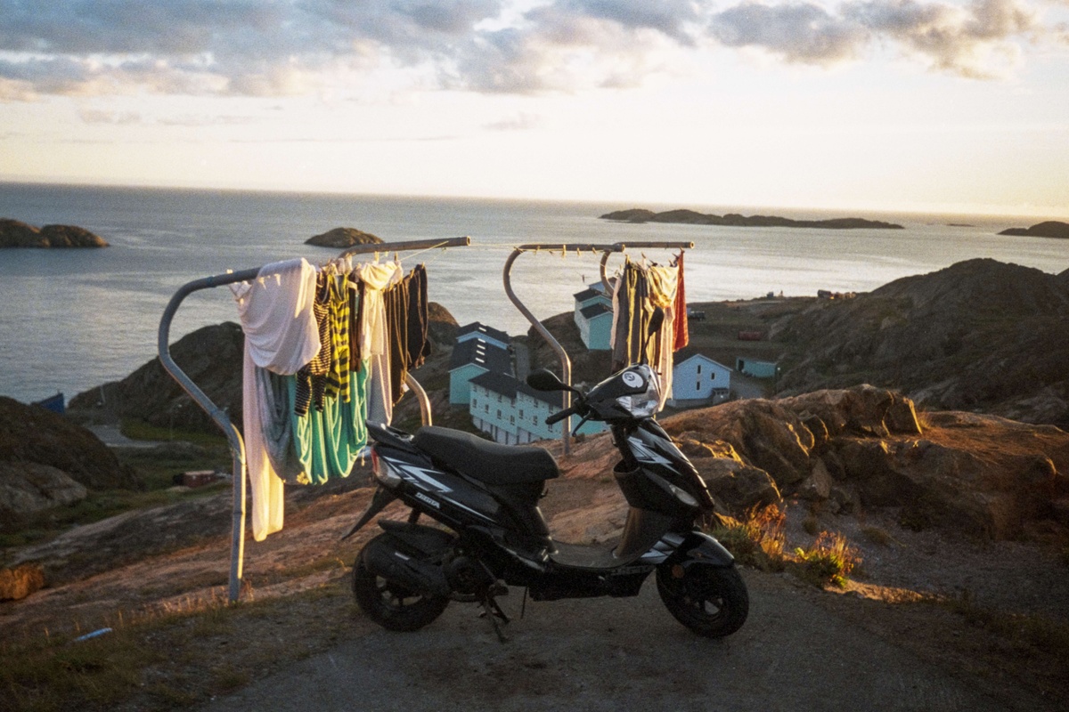 An electric scooter with wet clothes hanging over it is set against a sublime ocean landscape. photo by Inuuteq Storch